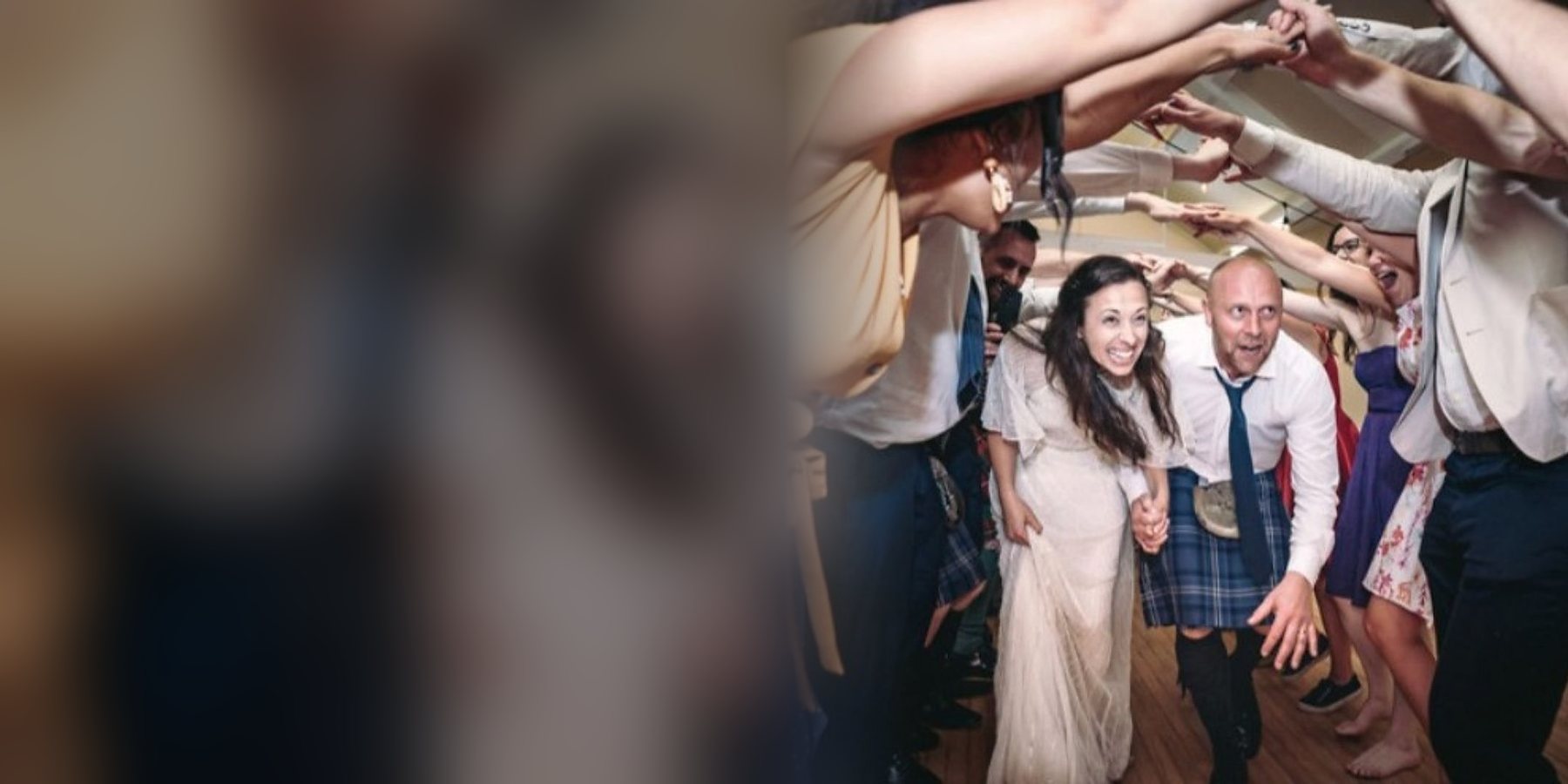 A bride and a groom in a kilt bursting through an arch of raised hands, guests cheering them on either side