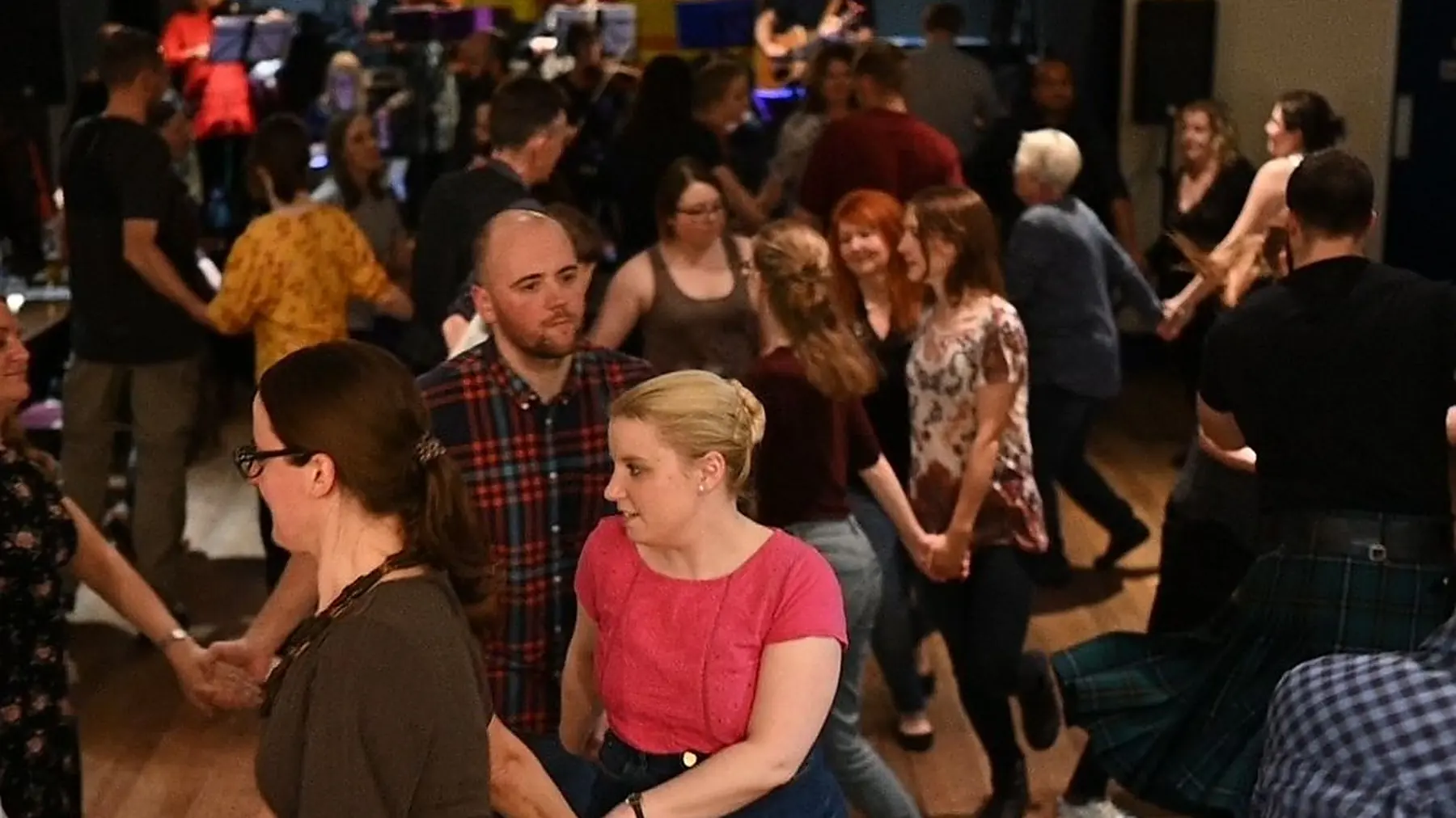 A busy club-night ceilidh in a hall, dancers of all ages hand in hand